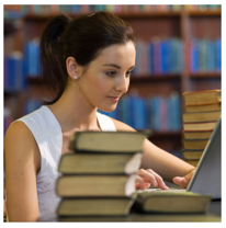 Female student typing on her computer, while surrounded by books.